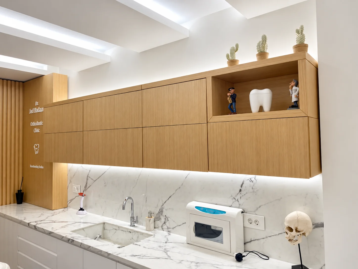 Pale wood cabinets, a marble worktop and dental models in the Hazmieh clinic, in an AI-enhanced clinic photograph.